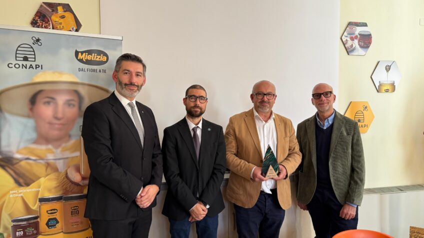 Quattro uomini posano con il trofeo del Generative Business Award davanti al banner CONAPI-Mielizia nella sede del consorzio a Monterenzio